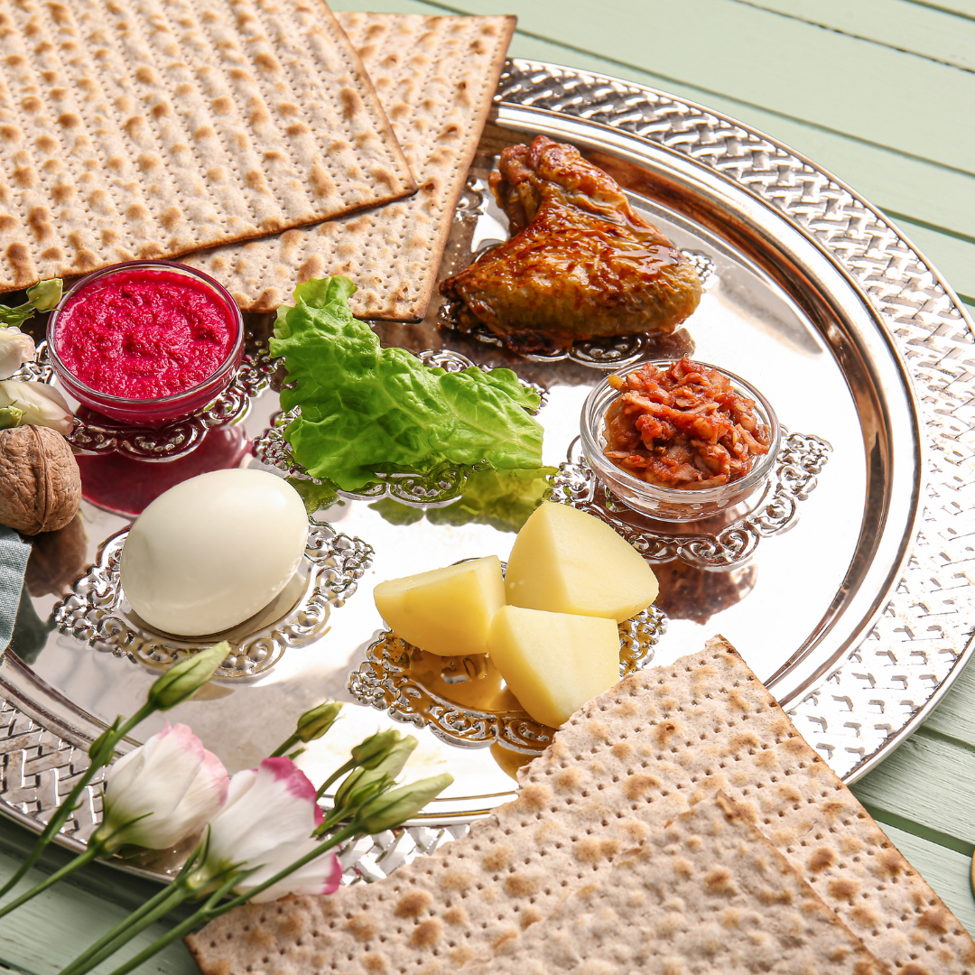 An elaborately set Passover Seder plate displaying traditional foods such as matzo, a shank bone, charoset, karpas vegetables, an egg, and bitter herbs, arranged on a decorative silver tray. 