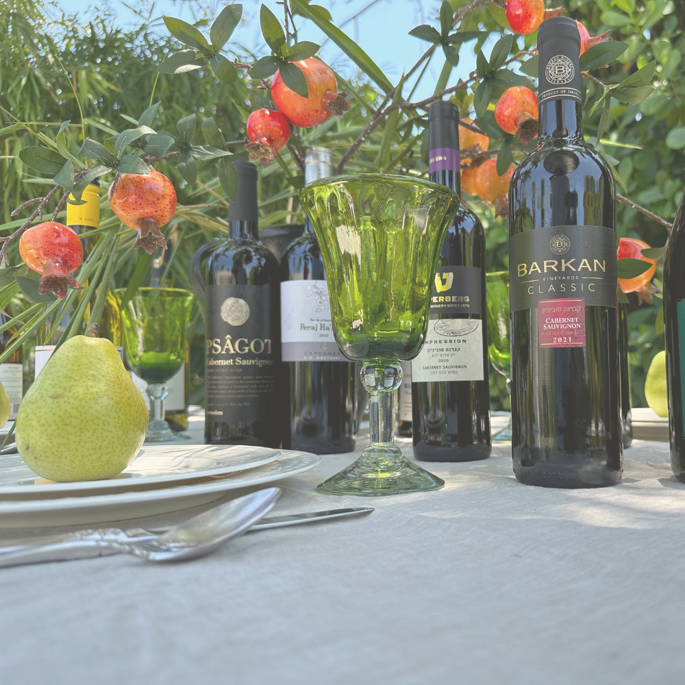 A table with kosher wine bottles, glasses, and a pear.