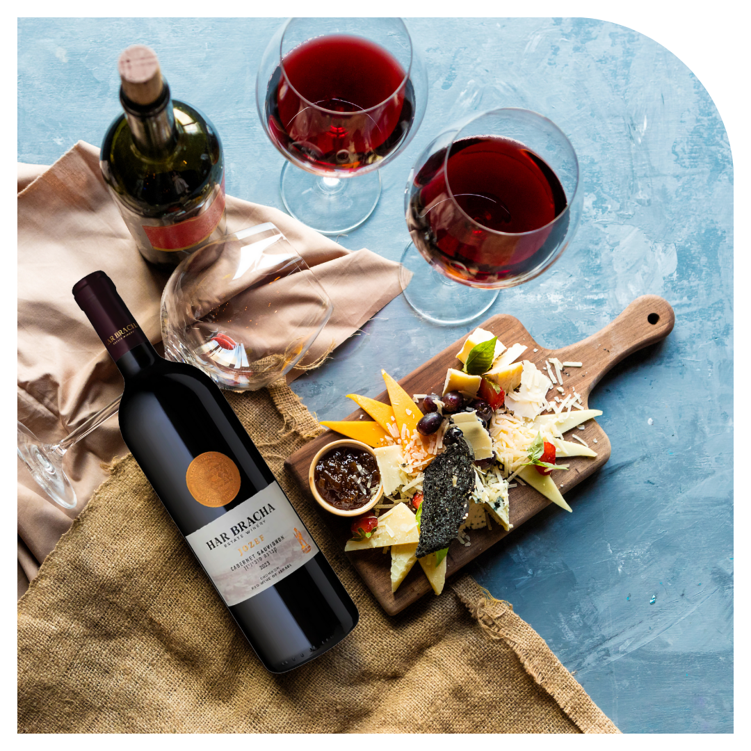 Wine bottle, two glasses of red wine, and a charcuterie board with food on a blue surface.