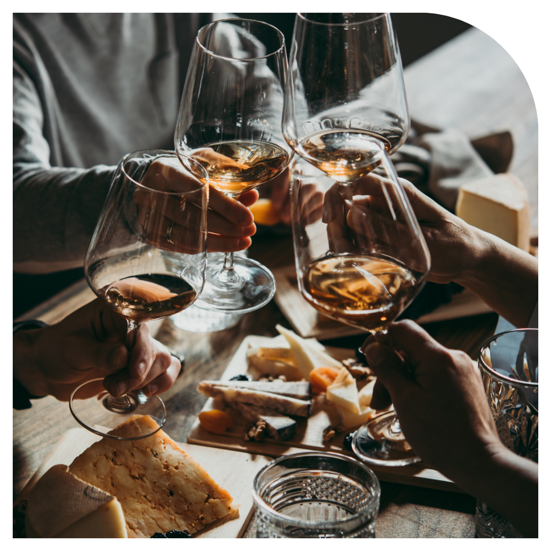 People toasting with wine glasses at a table with cheese and snacks.