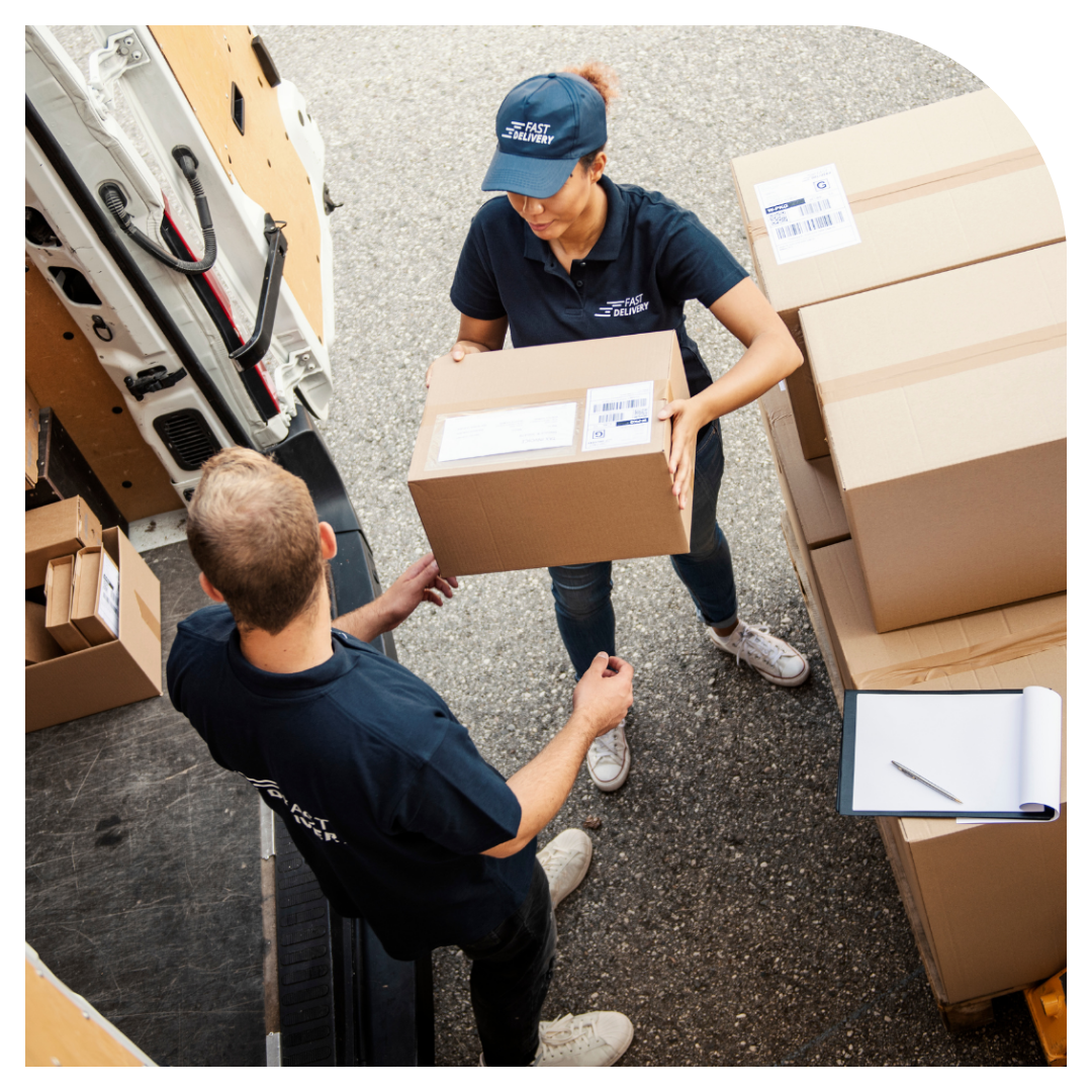 Two workers in a warehouse setting, one handing a box to the other.
