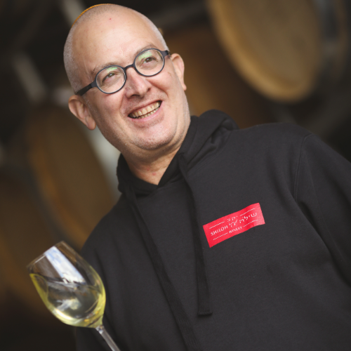 Amichai Lourie, smiling and wearing glasses and a black hoodie with a red 