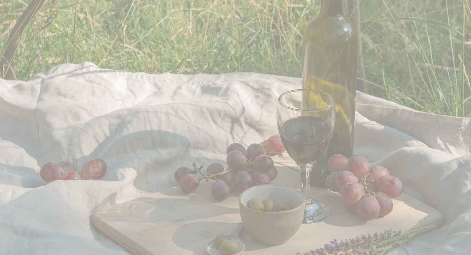 red wine bottle and glass with grapes laid out on a picnic blanket