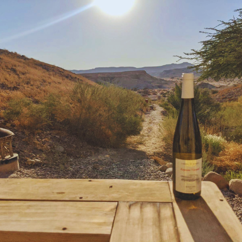 A bottle of wine on a wooden table with a scenic view of a sunlit path and hills in the background