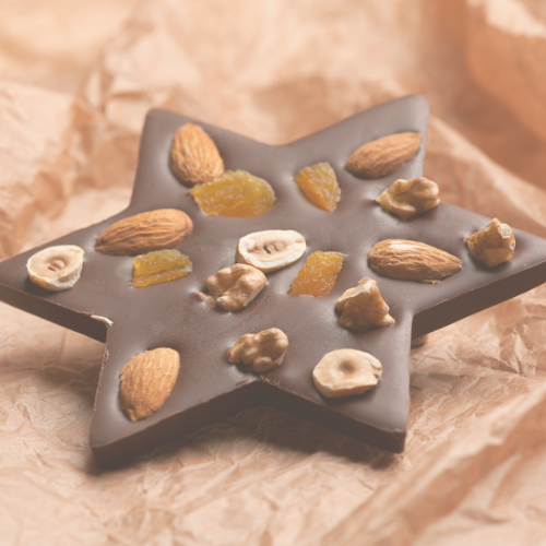 A dark chocolate bark in the shape of the Star of David, adorned with almonds, hazelnuts, and candied fruit on crinkled parchment paper.