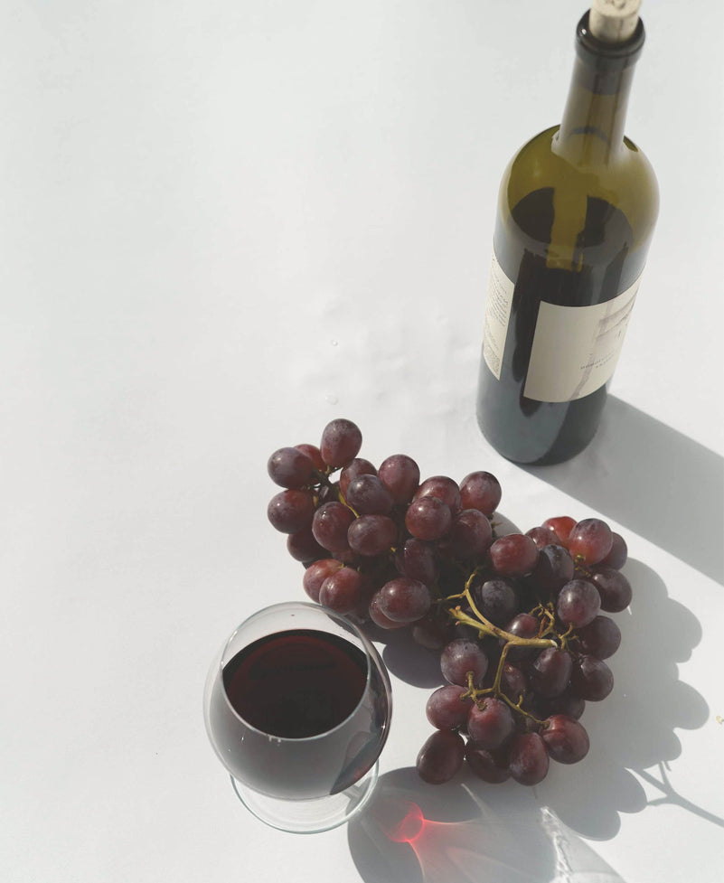 a glass and a bottle of cabernet sauvignon with grapes 