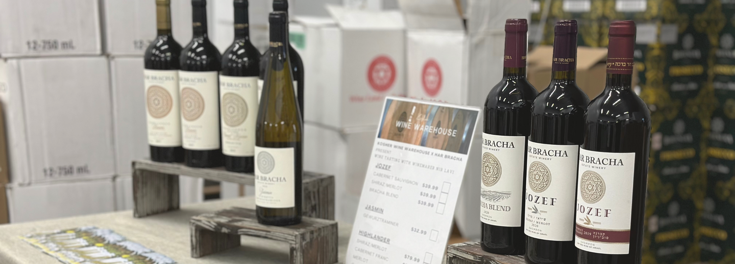  Bottles of Har Bracha wine are prominently displayed on wooden crates against a background of wine boxes in a storage warehouse.