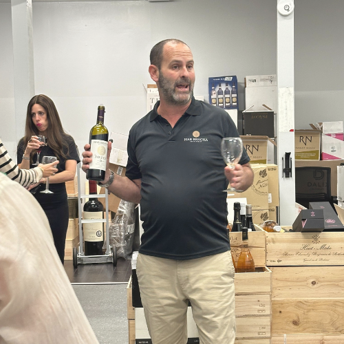 Har Bracha's owner Nir Lavi stands in a wine warehouse holding a bottle and a glass, with other attendees in the background.