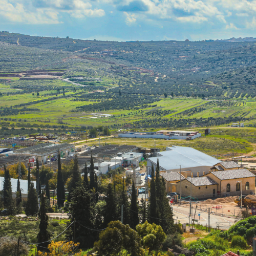 An aerial view of Shiloh Winery buildings surrounded by green hills and vineyards under a partly cloudy sky.