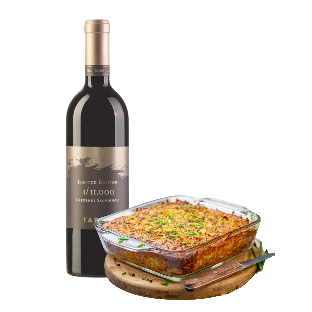 Bottle of limited edition red wine next to a dish of potato kugel on a white background