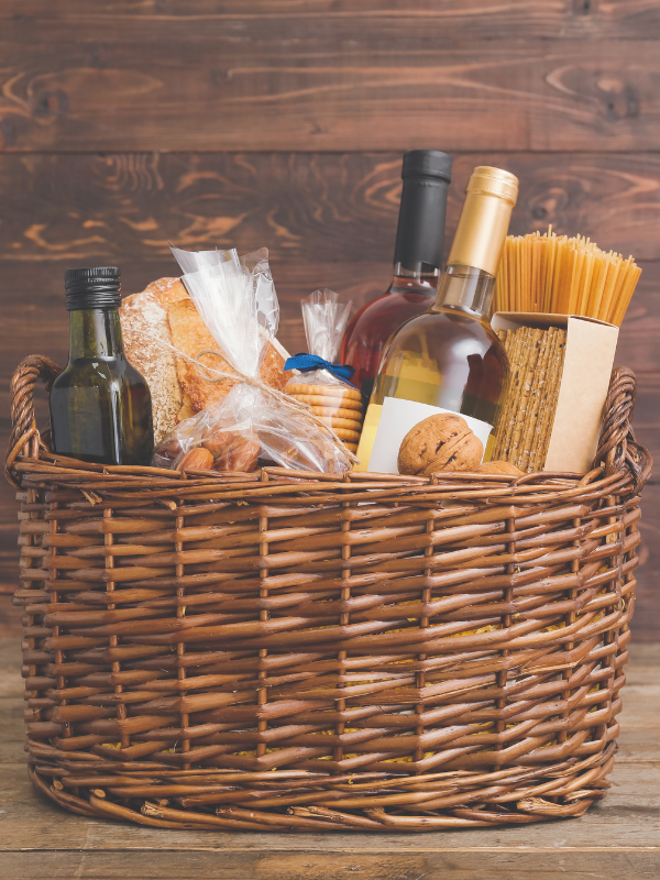 A wicker basket filled with wine bottles, bread, olive oil, cookies, and pasta, showcasing a variety of gourmet items.