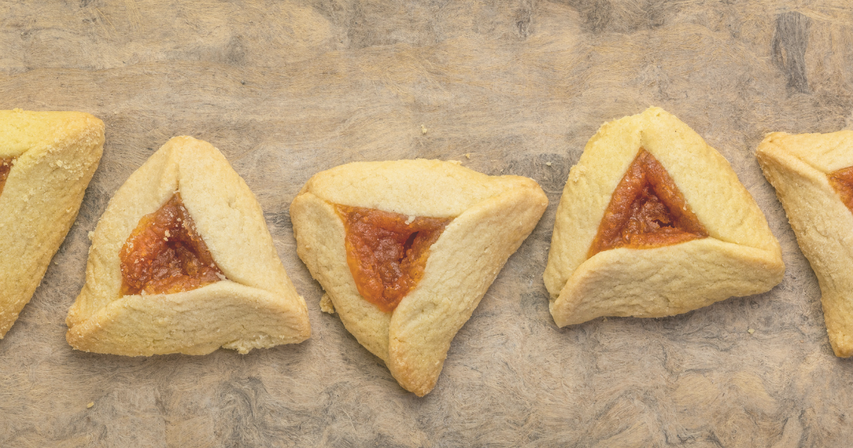 A row of golden-brown hamantaschen cookies with apricot filling on a rustic stone surface.