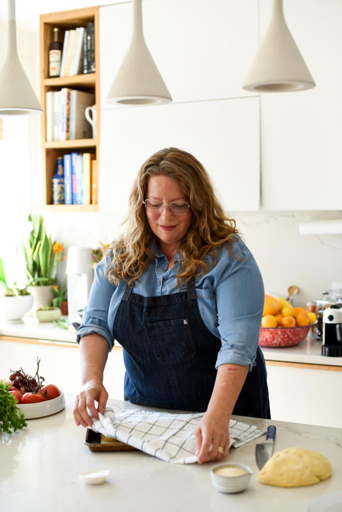 Adeena Sussman is wearing apron, preparing food in a kitchen.