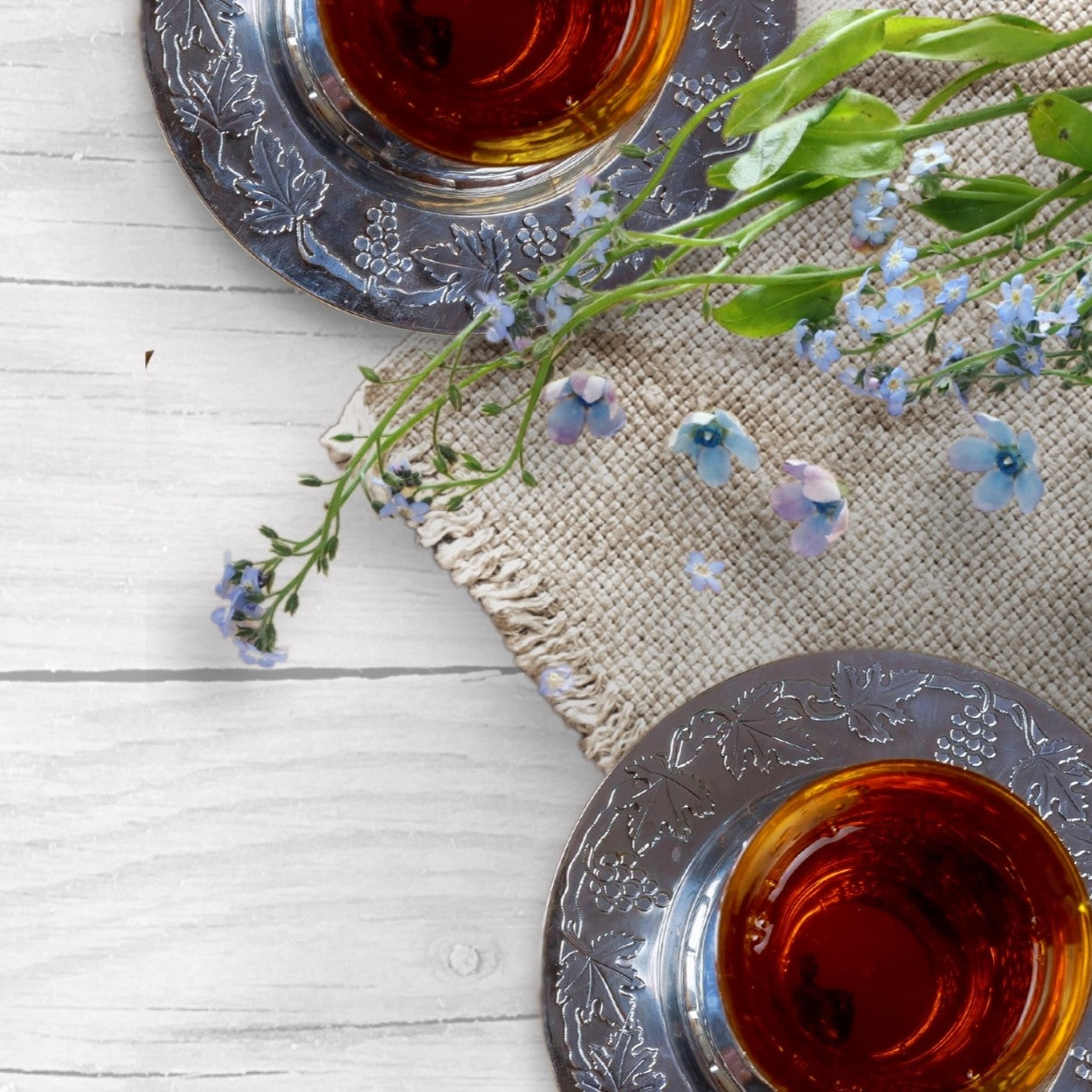 An elegant Passover setting with two glasses of red wine on a traditional silver tray, adorned with delicate blue flowers and placed on a natural woven placemat.