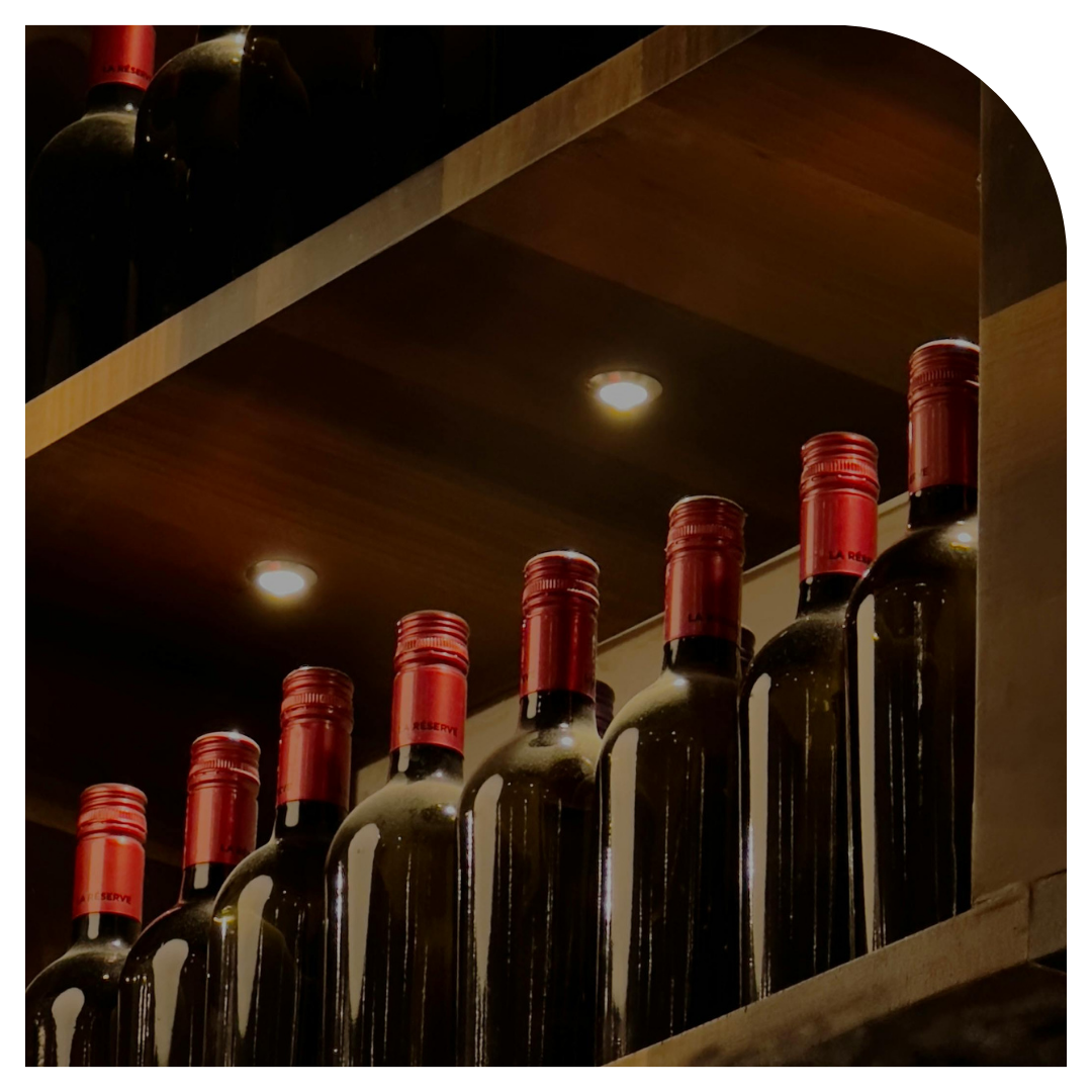 Row of wine bottles with red labels on a shelf in a dimly lit room.